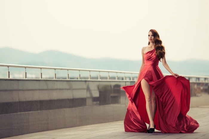 Beautiful woman in red fluttering dress. Urban background.